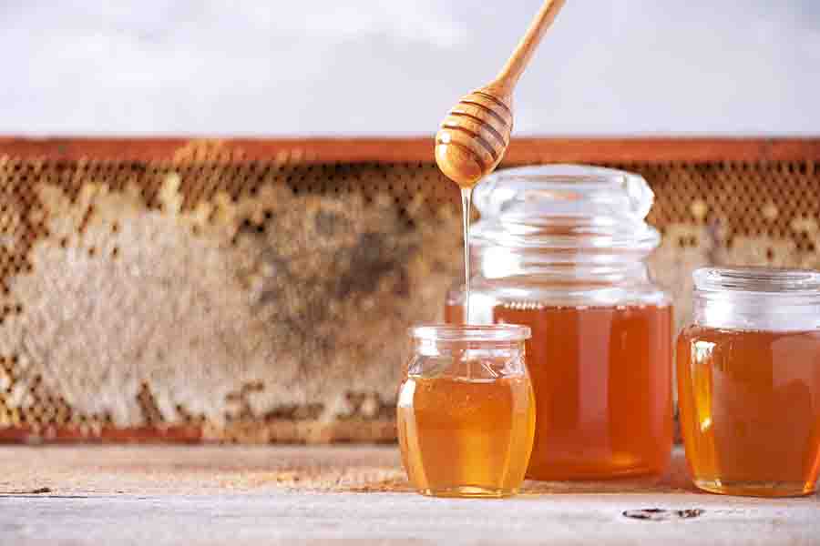 Miel goteando de una cuchara de miel de madera en un frasco sobre fondo gris.  Copie el espacio.  Concepto de cosecha de otoño.  Bandera
